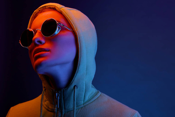 Neon portrait of young woman in round sunglasses and hoodie. Studio shot  - Foto, Bild