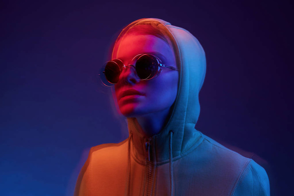 Neon portrait of young woman in round sunglasses and hoodie. Studio shot, 3d effect, motion.  - Foto, immagini