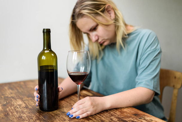 junge Frau, die zu Hause bei einem Glas Rotwein sitzt. Konzept für alkoholische soziale Probleme - Foto, Bild