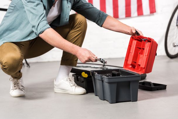 cropped image of man putting adjustable wrench in tools box  - Foto, afbeelding
