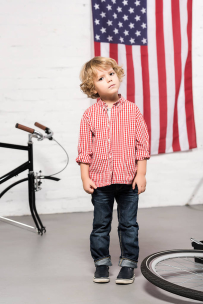 adorable niño mirando la cámara cerca de la bicicleta desmontada en el taller
 - Foto, imagen