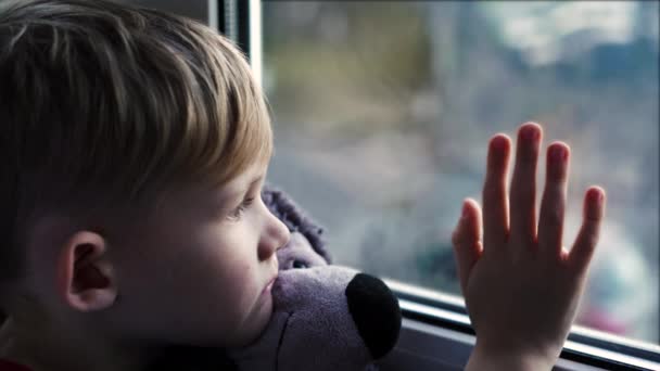 ein schöner kleiner blonder Junge schaut aus einem sonnigen Fenster und wartet auf ihren Papa, um von der Arbeit nach Hause zu kommen. - Filmmaterial, Video