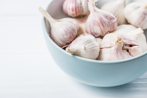 Garlic bulbs in blue ceramic bowl on white table - Фото, зображення