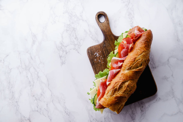 Fresh baguette sandwich banh-mi styled with ham and tomatoes with fresh lettuce on wooden cutting board  - Fotografie, Obrázek