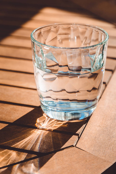A transparent glass of crystal clean water on the wooden table and beautiful sunlight, healthy drink, sunny day, closeup - Foto, Imagem