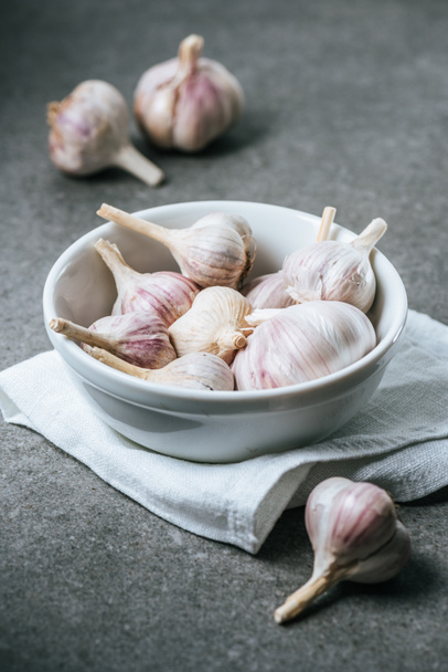 Garlic bulbs in ceramic bowl with white cloth on grey background - 写真・画像