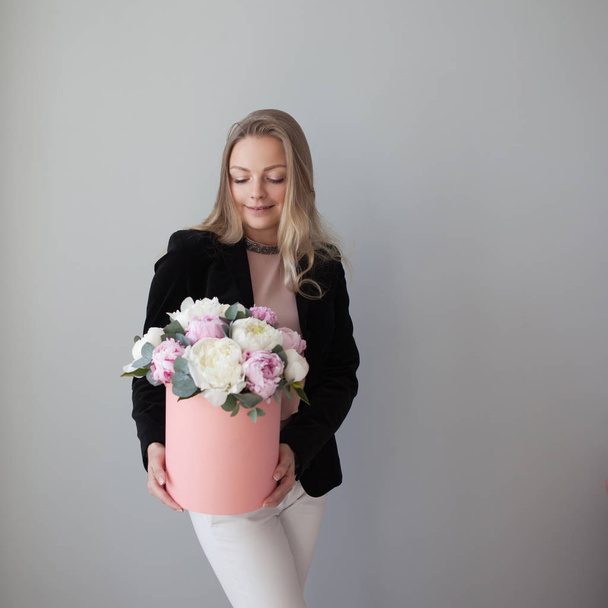 Charming blonde woman with flowers in a hat box. Bouquet of peonies. Girl in business style, receives flowers or gives - Foto, Bild