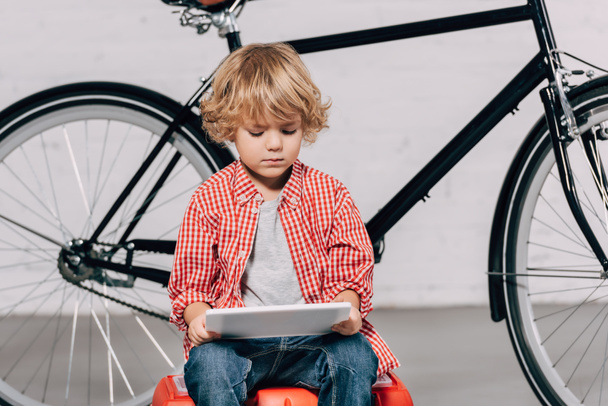 Selektivní fokus malého chlapce sedí na nářadí box a pomocí digitálního tabletu  - Fotografie, Obrázek
