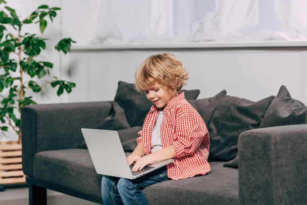 happy curly boy using laptop on sofa at home - Фото, изображение