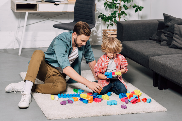 selective focus of child and his father playing with colorful plastic blocks on floor at home - Photo, Image