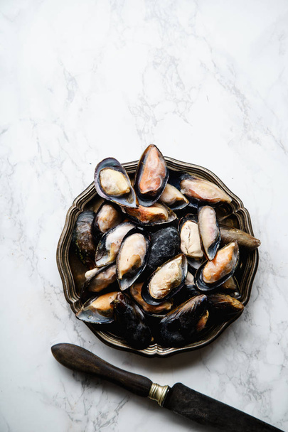 frozen mussels on vintage metallic plate on white marble background, top view  - Фото, изображение
