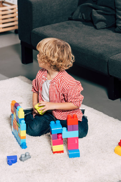 high angle view of curly little kid playing with colorful plastic blocks on floor at home - Fotografie, Obrázek