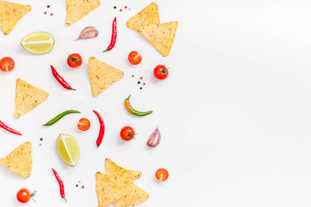 Creative Top view flat lay of fresh mexican food ingredients with tortilla nachos chips garlic pepper lime tomatoes on white table background with copy space. Food preparation cooking concept frame - 写真・画像