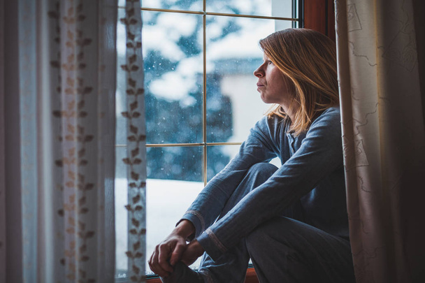 Λυπημένη γυναίκα που κάθεται δίπλα στο παράθυρο κοιτάζοντας έξω από - Φωτογραφία, εικόνα