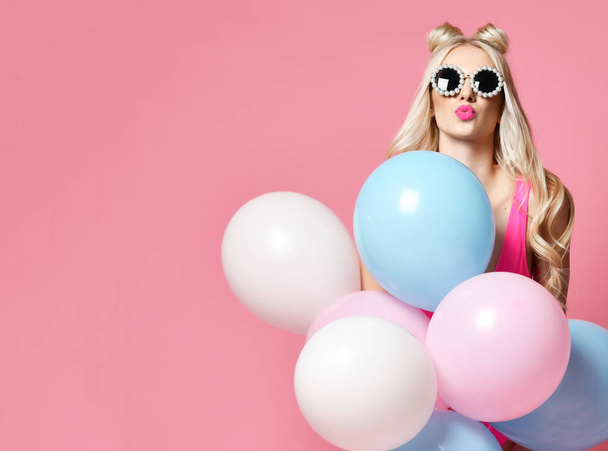 Blonde woman on birthday party having fun with pastel color air balloons blow kiss in round sunglasses  - Foto, immagini