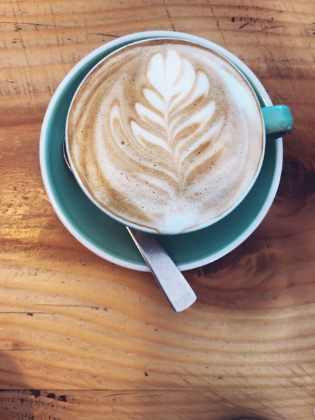 Café Cappuccino caliente decorado con hojas de árbol en leche Latte espuma arte espuma en taza taza azul sobre fondo de mesa de madera rústica. Relajado con bebidas lácteas saludables con dulces derretidos por la mañana
. - Foto, imagen