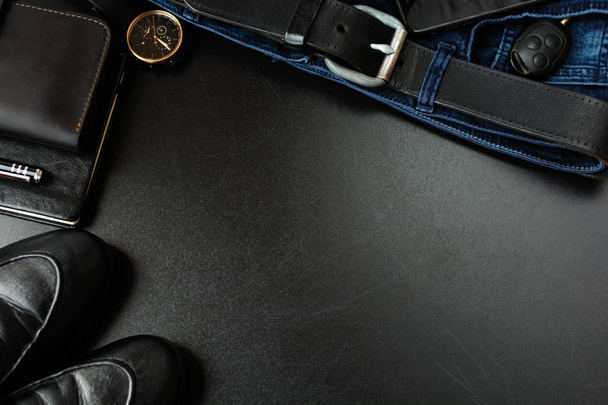 Men's accessories (notebook, pen, phone, shoes, wrist watches, wallet, purse, belt, jeans, pants, shoes) on a black board. - Photo, image