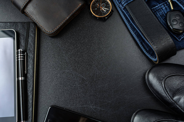 Men's accessories (notebook, pen, phone, shoes, wrist watches, wallet, purse, belt, jeans, pants, shoes) on a black board. - Photo, image