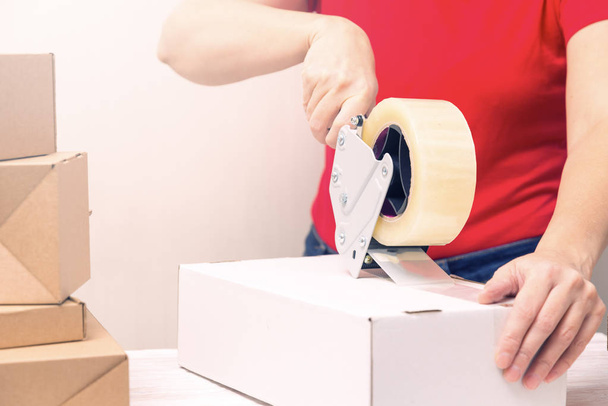 Woman packing cardboard boxes using tape dispenser - Foto, afbeelding