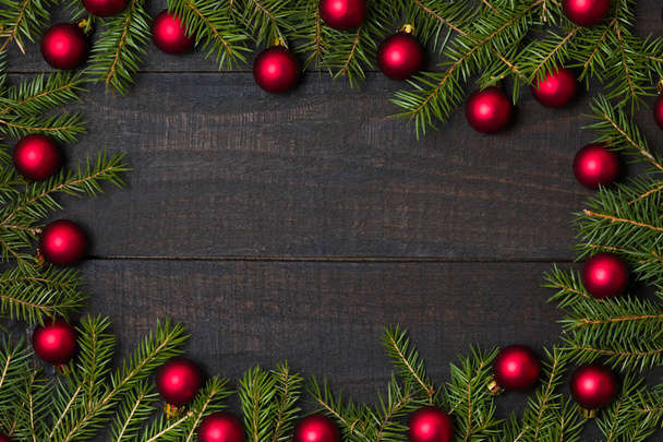 Dark rustic wood table flatlay - Christmas background with red ball ornament decoration and fir branch  frame. Top view with free space for copy text - Photo, Image