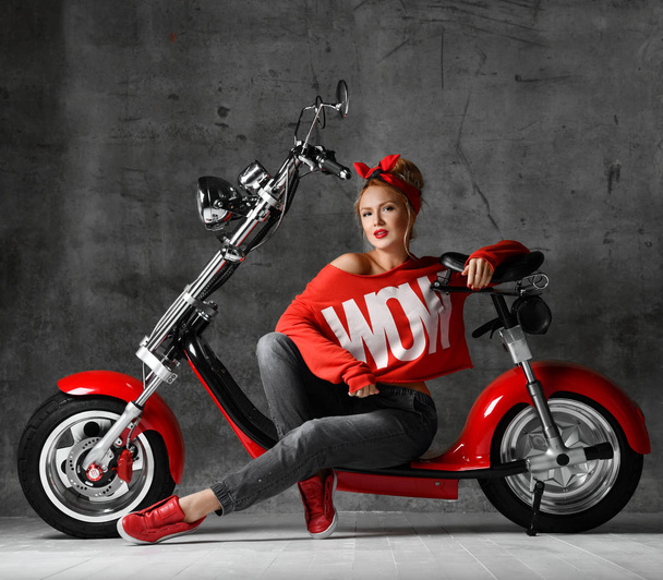 Woman sitting on motorcycle bicycle scooter  retro pinup style in red blouse and jeans  - Фото, изображение