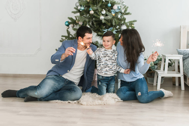Happy young happy family of three near the Christmas tree. Mother and father and son lit the lights. Happy parenting concept. New Year's interior - Foto, Bild