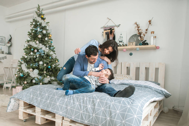 Happy family at Christmas together in bed together near a tree. The concept of family happiness and well-being. - Zdjęcie, obraz