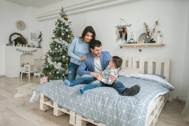 Happy family at Christmas together in bed together near a tree. The concept of family happiness and well-being. - Photo, Image