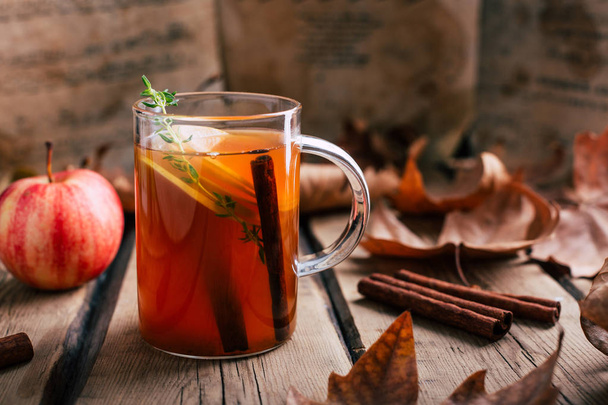Apple tea, cinnamon sticks, wooden background, retro rustic style, autumn mood, fallen dry leaves - Photo, Image