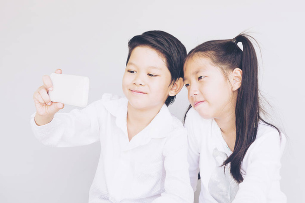 Lovely Asian couple school kids are taking selfie, 7 and 10 years old, over gray background - Fotografie, Obrázek
