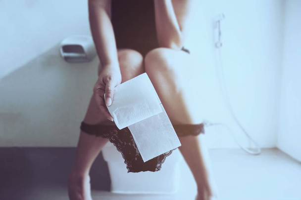Woman sitting on toilet bowl holding tissue paper  - health problem concept - Foto, afbeelding