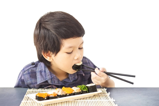Asian lovely boy is eating sushi isolated over white background - 写真・画像