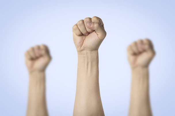 Mãos masculinas apertadas em um punho e levantadas sobre um fundo azul. Conceito de poder, rebelião, unidade, revolução, motim
. - Foto, Imagem