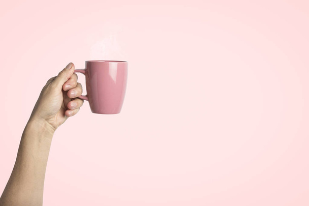 Mannelijke hand met een paarse kop met warme koffie of thee op een lichte roze achtergrond. Ontbijt concept met warme koffie of thee. - Foto, afbeelding