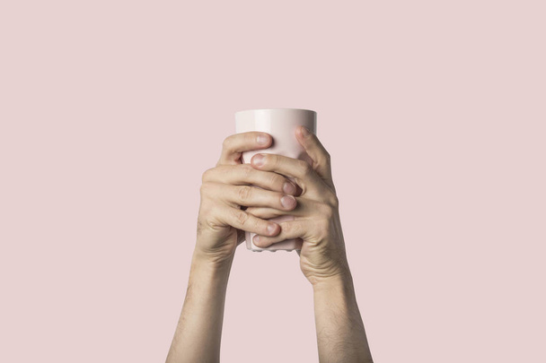 Male hand holding a purple cup with hot coffee or tea on a light pink background. Breakfast concept with hot coffee or tea. - Photo, Image
