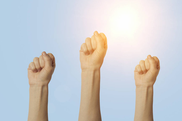 Les mains féminines serrées dans un poing et levées sur un fond bleu. Concept de pouvoir, rébellion, unité, révolution, émeute
. - Photo, image