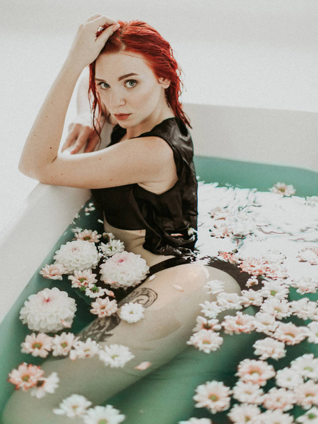 Portrait of a beautiful redhead girl taking bath, blue water and flowers - 写真・画像