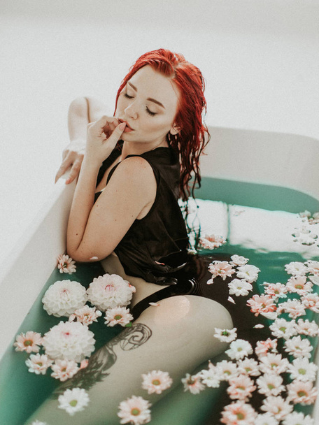 Portrait of a beautiful redhead girl taking bath, blue water and flowers - Φωτογραφία, εικόνα