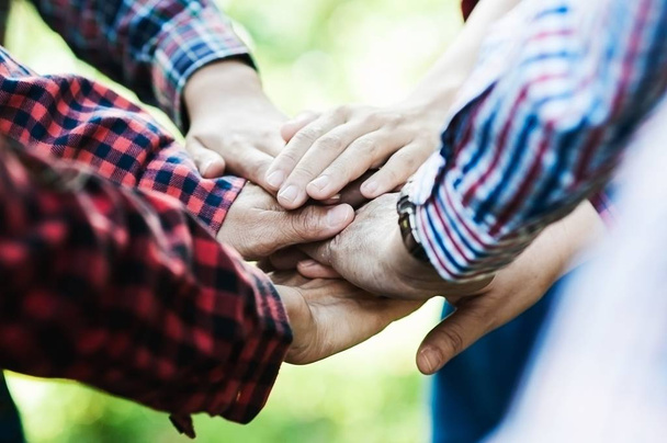 People group join hands together as teamwork unity symbol during their meeting activity to achieve their ultimate goal. Vintage tone close up at join hands over blur soft light green garden background - Photo, Image