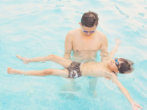 Asian father teaching son in swimming pool - Photo, Image