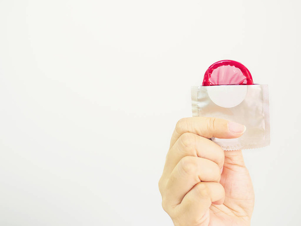 Lady's hand showing red condom and package with white copy space background - 写真・画像