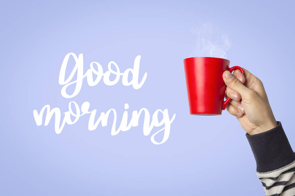 Kırmızı bir fincan sıcak kahve veya çay mavi bir arka plan üzerinde tutan erkek el. Metin Günaydın ekledi. Sıcak kahve ile kahvaltı konsepti. - Fotoğraf, Görsel