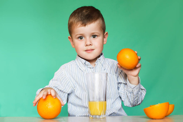 Little boy with oranges and juice. Happy little boy drinking orange juice on green backgraund - Photo, Image