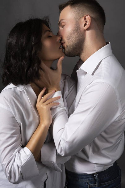 Closeup of a beautiful couple wearing white shirts. The girl and the man passionately almost touch their lips to each other. Casual style. Lifestyle, fashion, commercial design. Gray background. - Фото, зображення