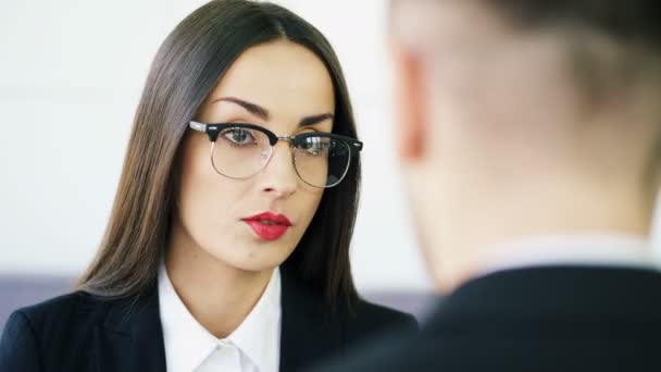 4k. Höfliche junge Brünette, Geschäftsfrau, spricht im Büro mit Mann. Gesicht hautnah in Brille - Filmmaterial, Video