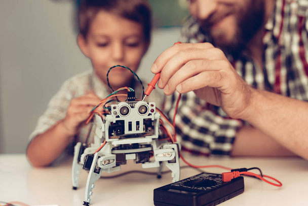 Bearded Father and Son Constructing Robot at Home. Young Boy in Shirt. Indoor Joy. Modern Hobby Concept. Modern Technology. Robot Engineering Concept. Bearded Young Man. Innovation for Fun. - 写真・画像