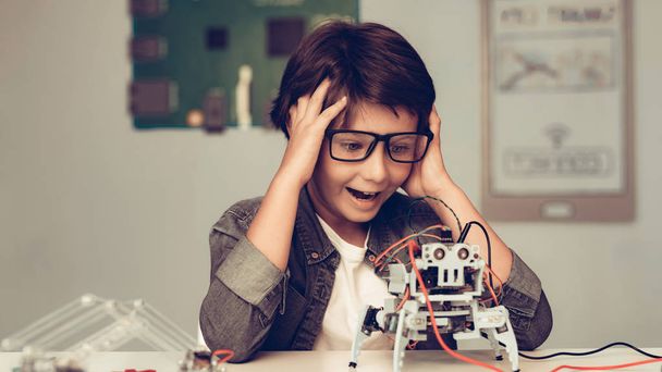 Boy Sitting at Desk and Constructing Robot at Home. Young Boy in Shirt. Indoor Joy. Modern Hobby Concept. Modern Technology. Robot Engineering Concept. Teenager with Robor. Innovation for Fun. - Foto, imagen