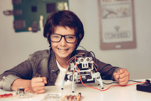 Boy Sitting at Desk and Constructing Robot at Home. Young Boy in Shirt. Indoor Joy. Modern Hobby Concept. Modern Technology. Robot Engineering Concept. Teenager with Robor. Innovation for Fun. - Zdjęcie, obraz