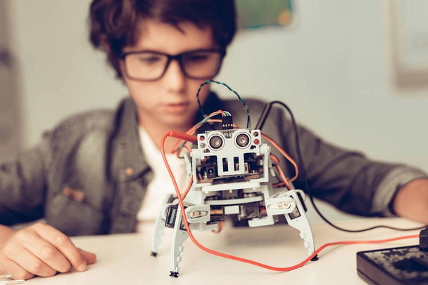 Boy Sitting at Desk and Constructing Robot at Home. Young Boy in Shirt. Indoor Joy. Modern Hobby Concept. Modern Technology. Robot Engineering Concept. Teenager with Robor. Innovation for Fun. - Foto, Imagem