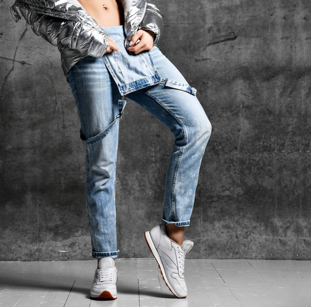 Sport woman legs in blue jeans in silver thin down puffer jacket white sneakers - Foto, Imagem